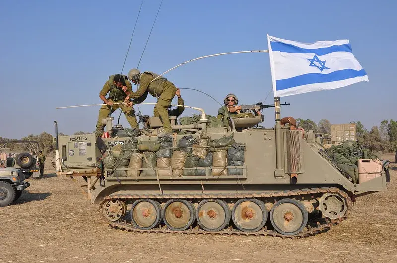 Armored tank with three soldiers in the top and a flag of Israel.