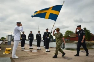 Military salute, with the Sweden flag behind.