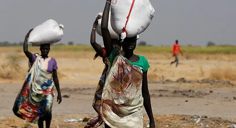 Sudanese people carrying food aid over their heads.
