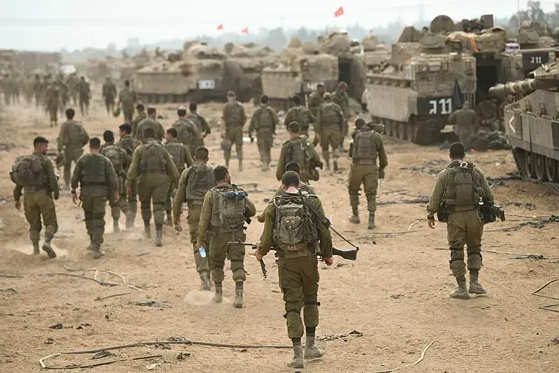 IDF soldiers walking in the desert next to a line of tanks.